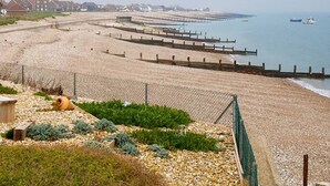 Une plage côtière avec une clôture, un petit bateau et des bâtiments en arrière-plan.