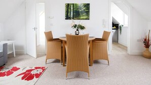 Un coin repas avec une table blanche et des chaises en osier, un lustre et une décoration murale sur le thème de la forêt.