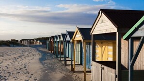 A row of beach huts along a sandy beach with a clear sky. - Pretty Coastal Home in Bosham Close to Water (Chichester)