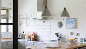 Une cuisine moderne dotée d’un îlot central, de luminaires suspendus et offrant une vue à travers une porte vitrée.
