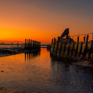 A sunset over a calm body of water with a pier and a satellite dish. - Pretty Coastal Home in Bosham Close to Water (Chichester)