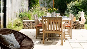 Une terrasse extérieure avec une table et des chaises en bois, un parasol blanc et un fauteuil en osier.