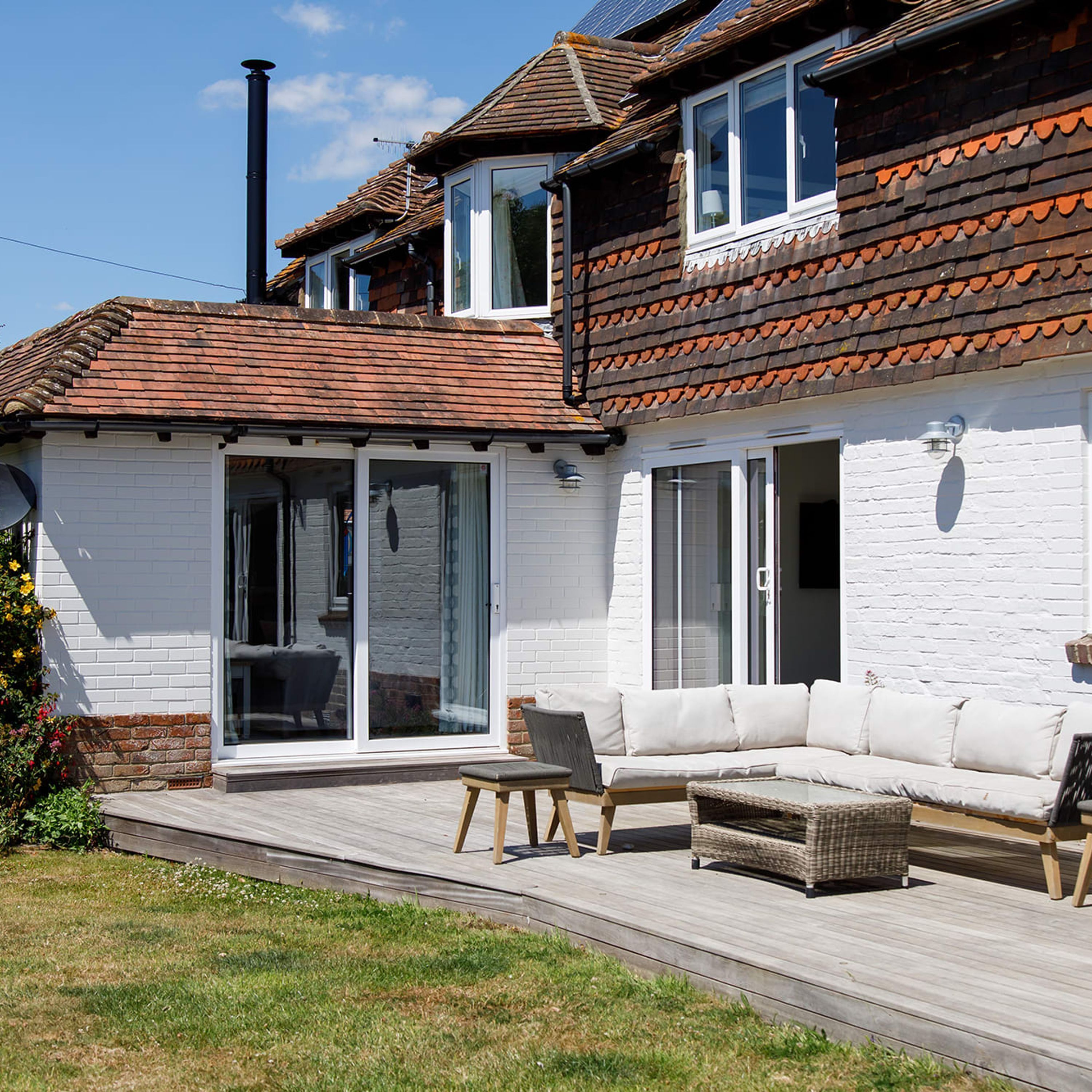 A two-story house with a white exterior, a tiled roof, and a wooden deck.