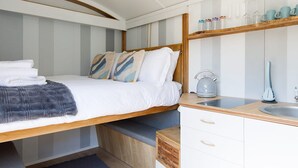 A compact bedroom with a bed, bedside tables, a small kitchenette, and a built-in shelf with kitchenware.