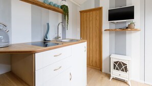 A kitchen with a wooden countertop, white cabinets, a sink, and a television mounted above it.