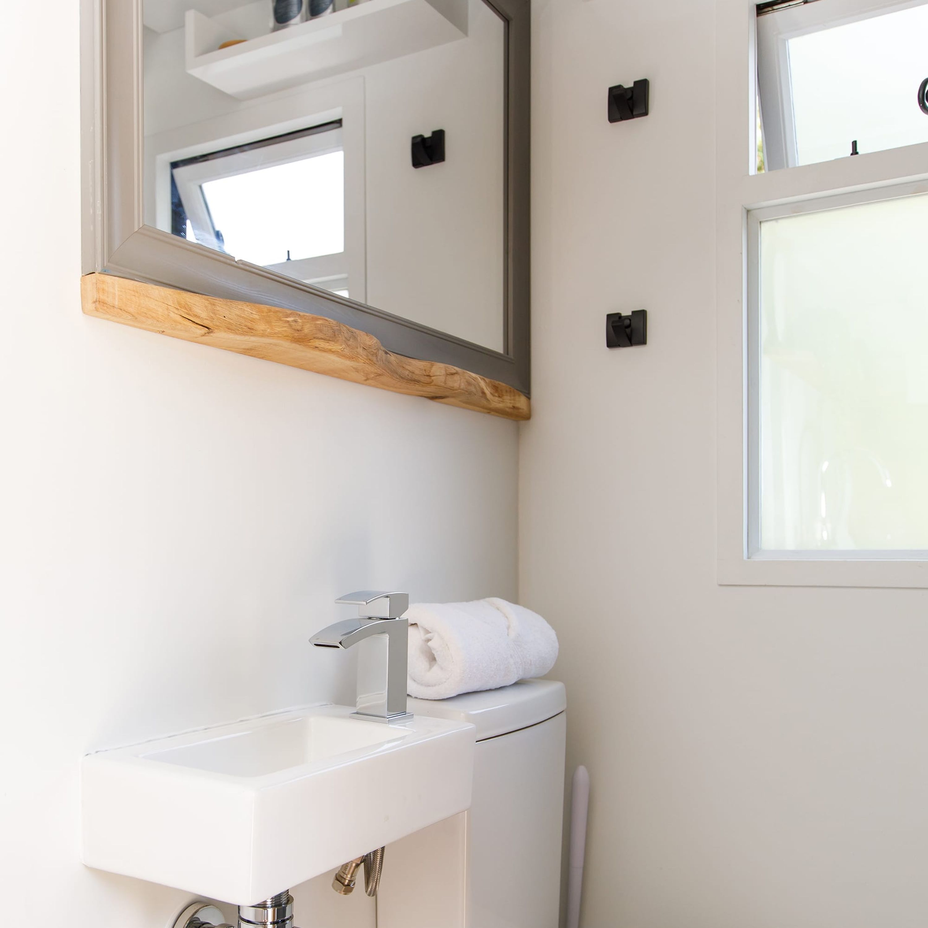 A bathroom with a white sink, a mirror with a wooden shelf, and a towel on the wall.