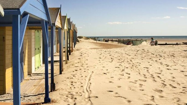 Une rangée de cabanes de plage, avec une plage de sable et la mer en arrière-plan.