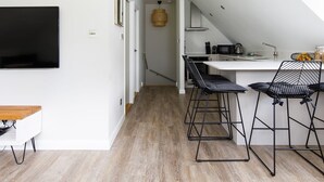 Une cuisine moderne avec un coin repas, comprenant un téléviseur, une table à manger en bois et des tabourets de bar noirs.