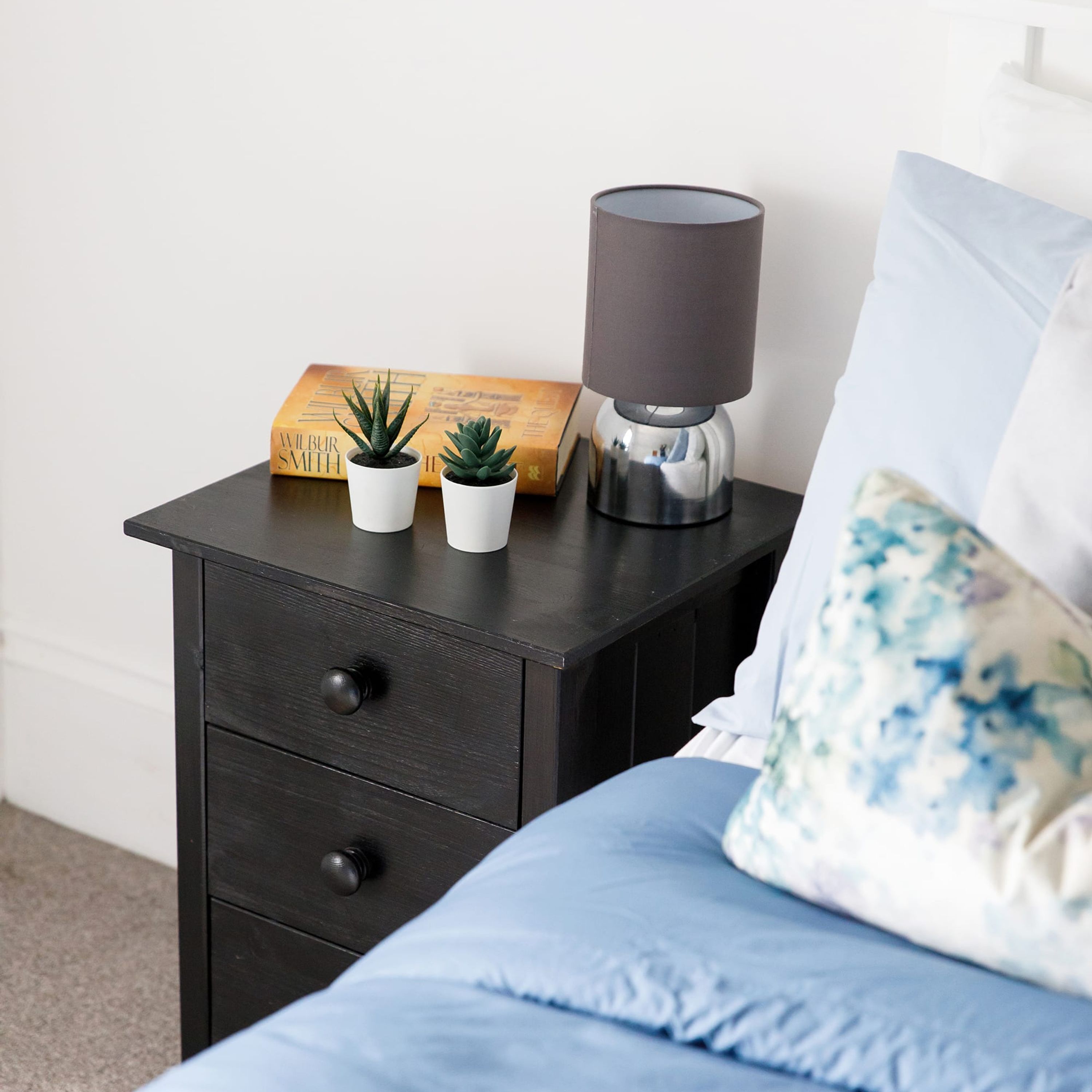 A dark wooden nightstand with two small potted plants, a lamp, and a book.