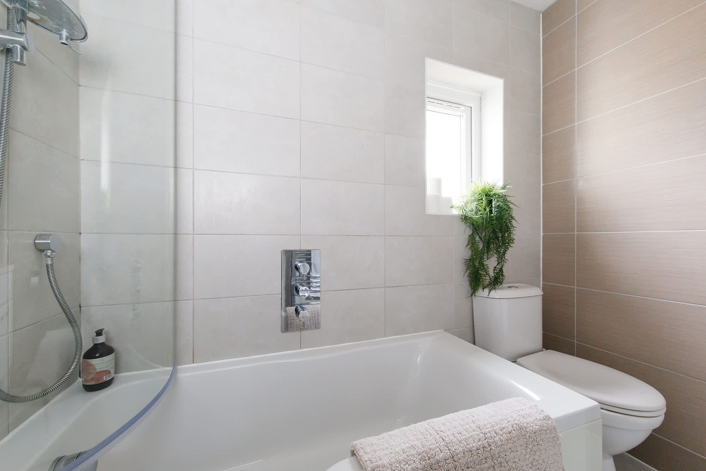 A modern bathroom with a bathtub, toilet, and a small window with a plant.
