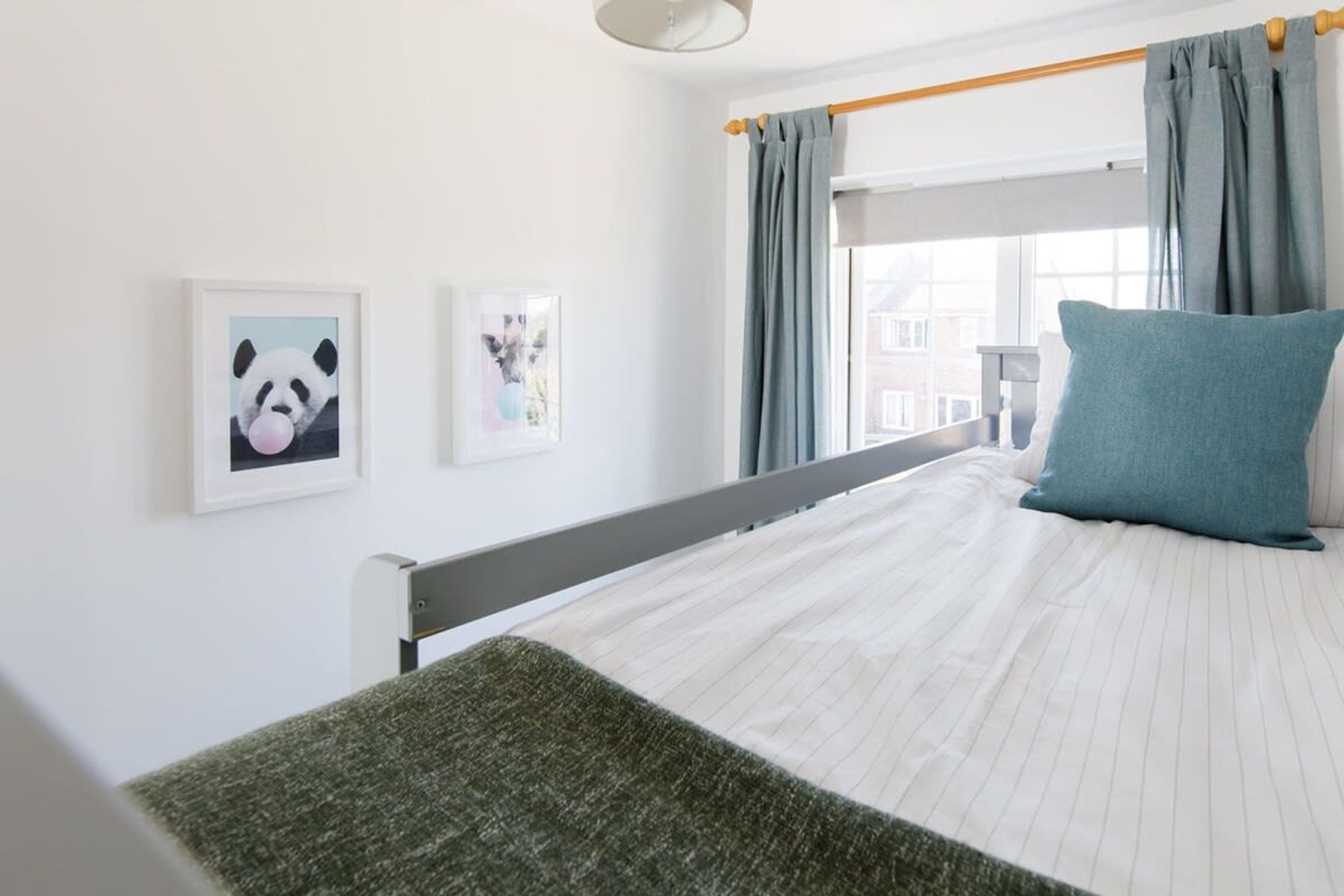 A bedroom with a bed, a window with curtains, and two framed pictures on the wall.