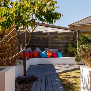 A covered outdoor seating area with colorful cushions, a wooden deck, and a tree. - Newly Refurbished Seaside Escape - 5 Mins to Beach (Chichester)