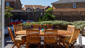 A wooden deck with a round table and chairs, surrounded by a wooden fence and greenery. - Newly Refurbished Seaside Escape - 5 Mins to Beach (Chichester)