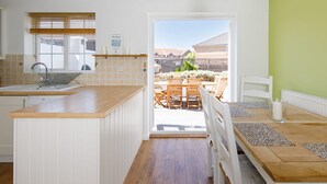 A modern kitchen with a wooden island, a dining area with a table and chairs, and a view of a backyard with a patio. - Newly Refurbished Seaside Escape - 5 Mins to Beach (Chichester)