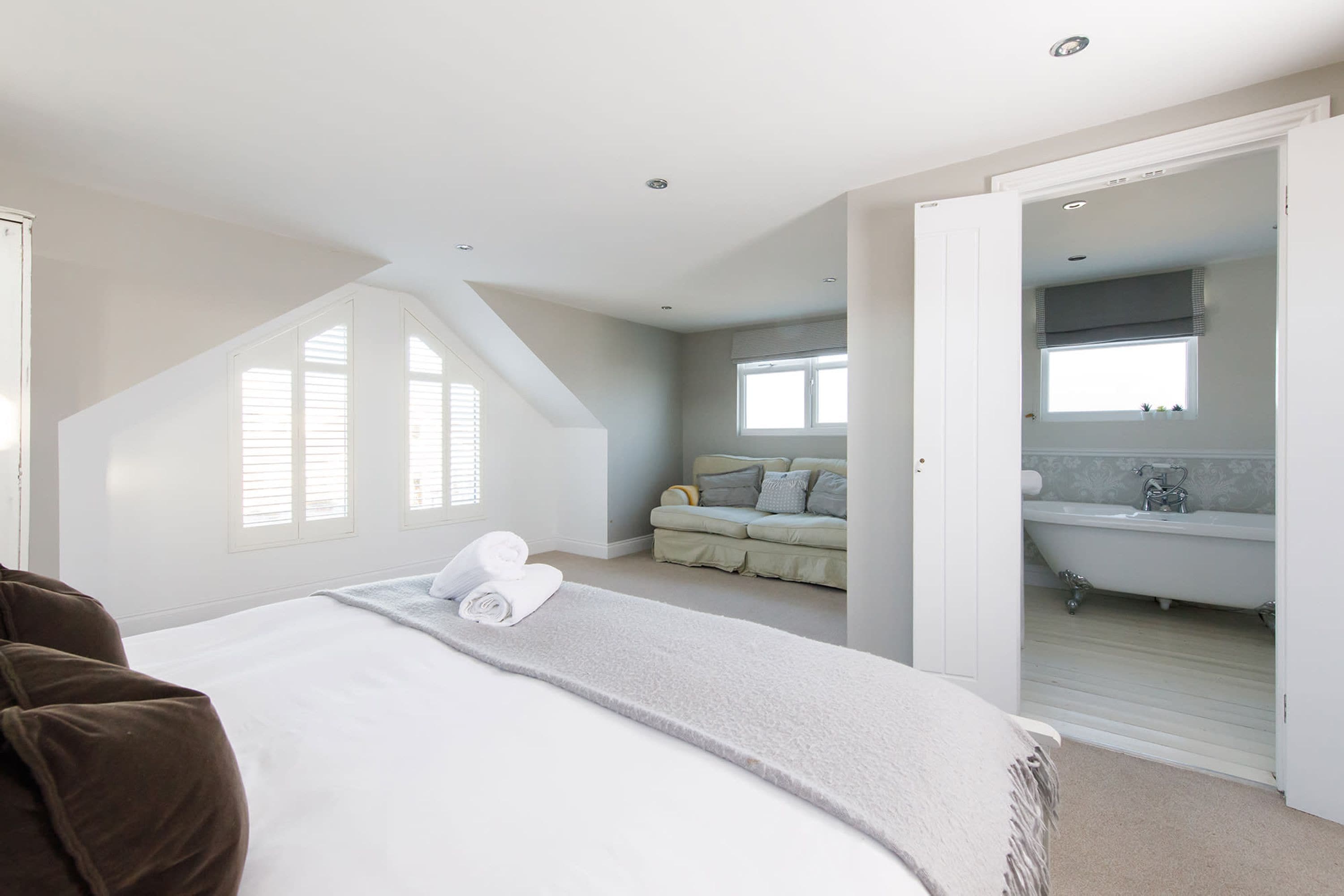 A bedroom with a large bed, a window, a sofa, and a bathroom visible through an open door.