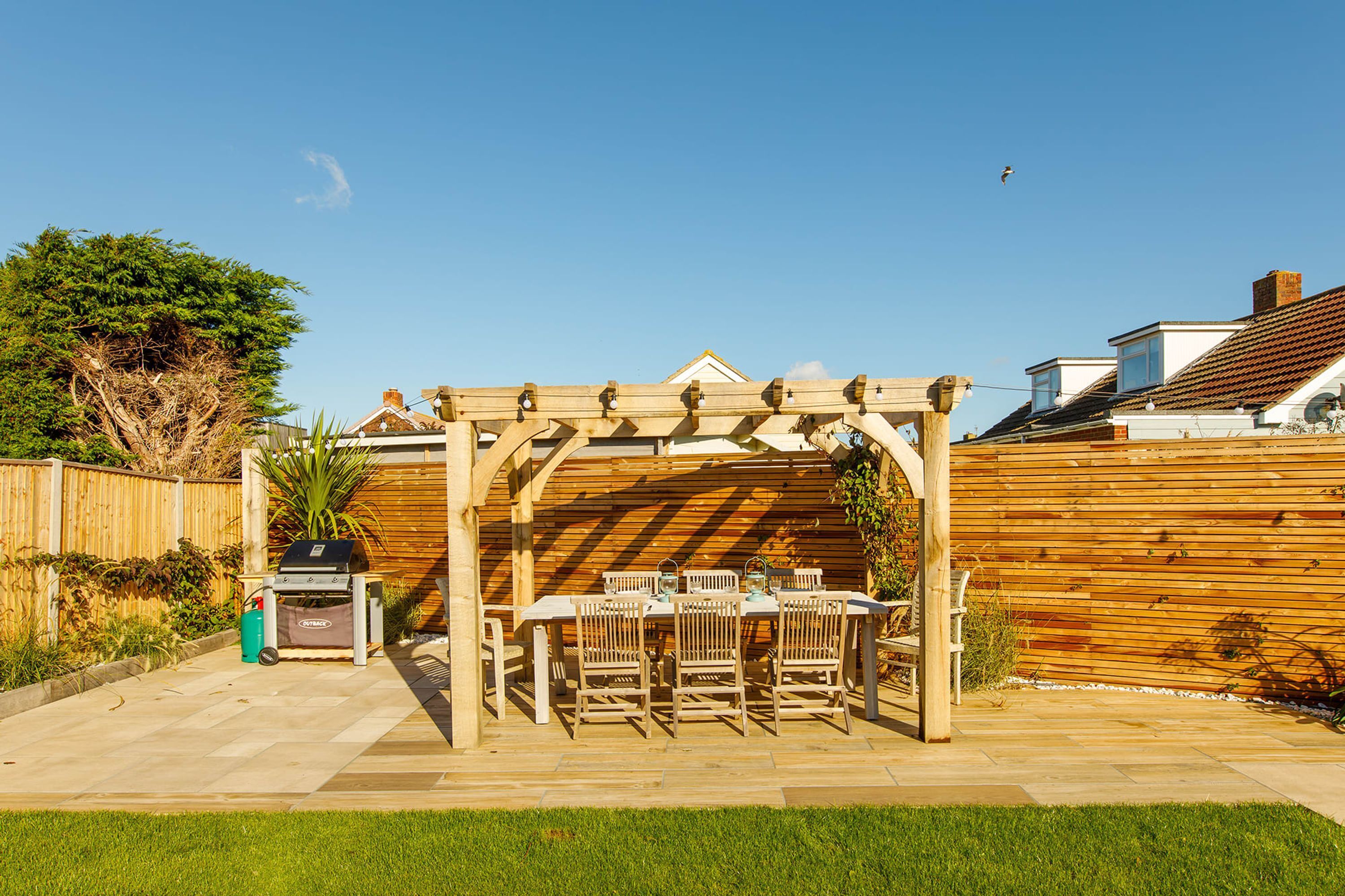 A wooden pergola with a table and chairs in a backyard.