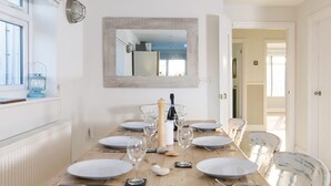 Un coin repas avec une table en bois dressée pour six personnes, des assiettes blanches, des verres à vin et un chandelier en guise de décoration centrale.