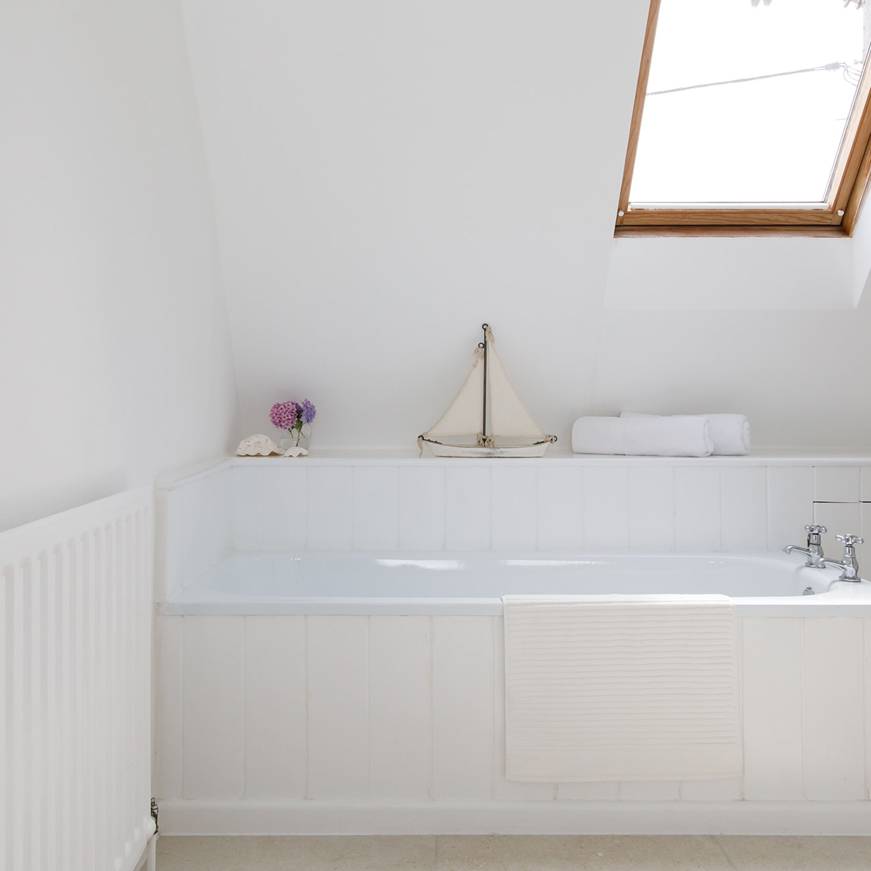 A white bathroom with a large bathtub, a window above the tub, and a radiator on the left.