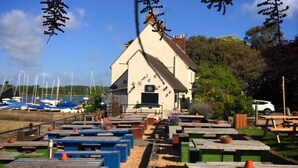 Un bâtiment à la façade blanche et au toit en pente, entouré d’espaces extérieurs aménagés avec des tables et des bancs.