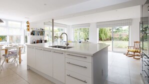 Une cuisine moderne avec des meubles blancs, un grand îlot central doté d’un évier et un coin repas comprenant une table et des chaises.