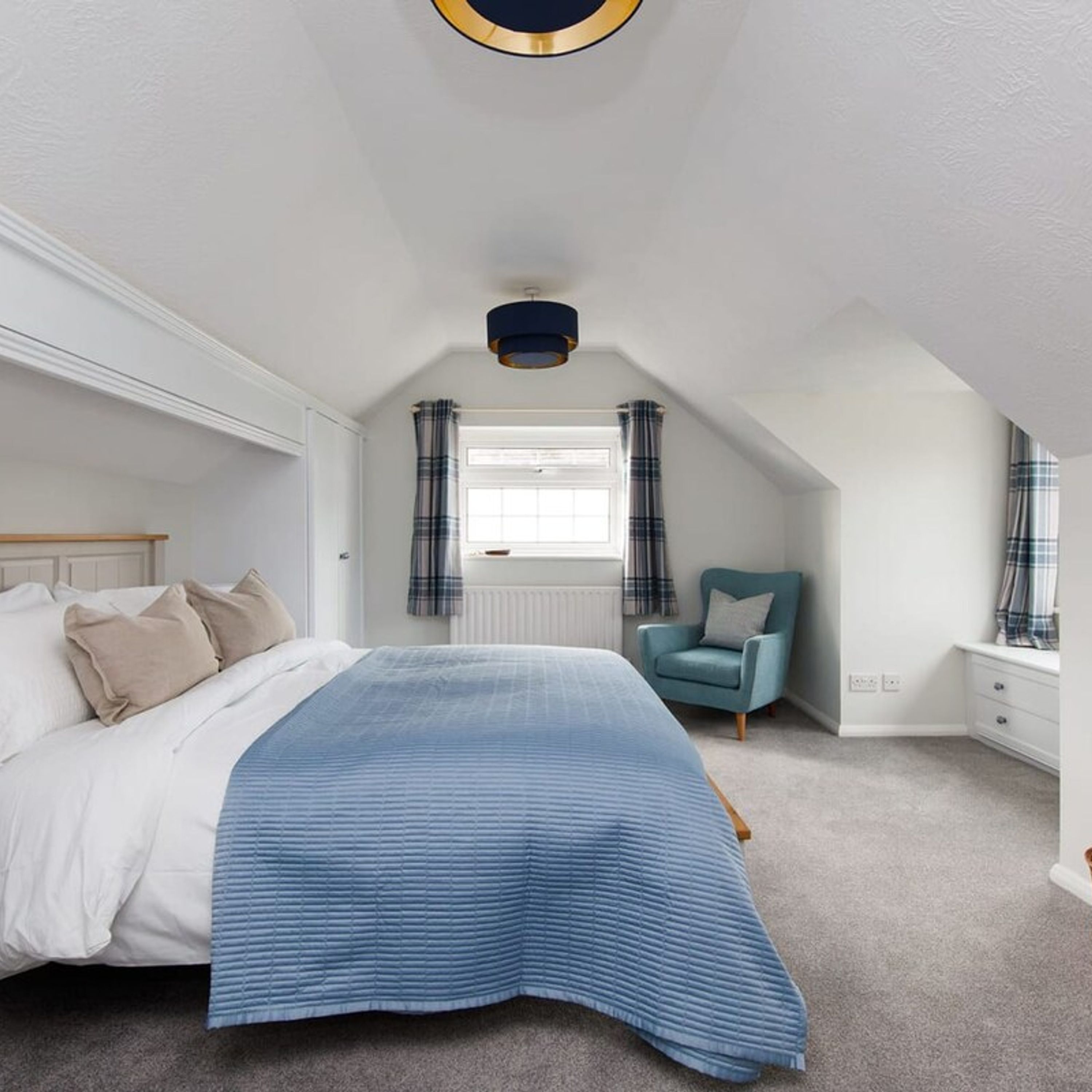 A bedroom with a bed, a chair, a window with curtains, and a ceiling light fixture.