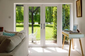 A room with a white sofa, a desk with a computer, and a sliding glass door leading to a garden.