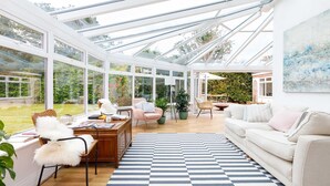 A spacious conservatory with large glass windows, a checkered rug, and a white sofa. - Stunning 5BR Home With Pool - 5 min to Beach (Chichester)