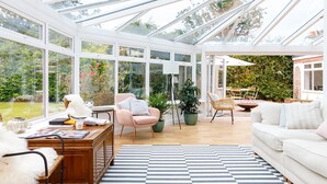 A spacious conservatory with a checkered floor, wooden furniture, and a view of the garden. - Stunning 5BR Home With Pool - 5 min to Beach (Chichester)
