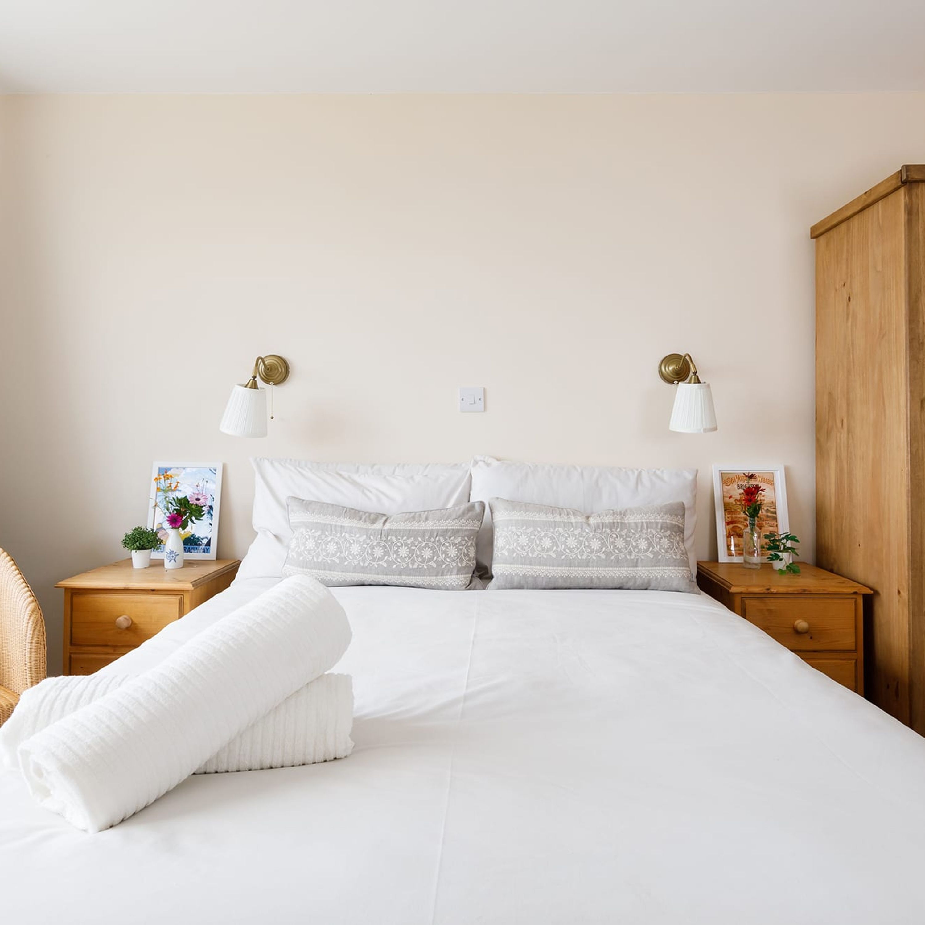 Una cama bien hecha con ropa blanca y almohadas decorativas, dos mesitas de noche con lámparas y un armario de madera.