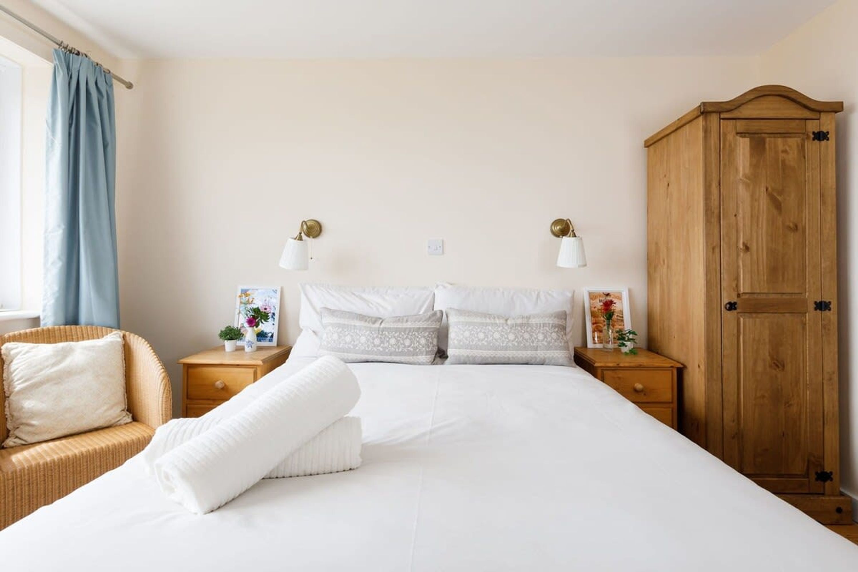 A bedroom with a large bed, two bedside tables, a wooden wardrobe, and a wicker chair.