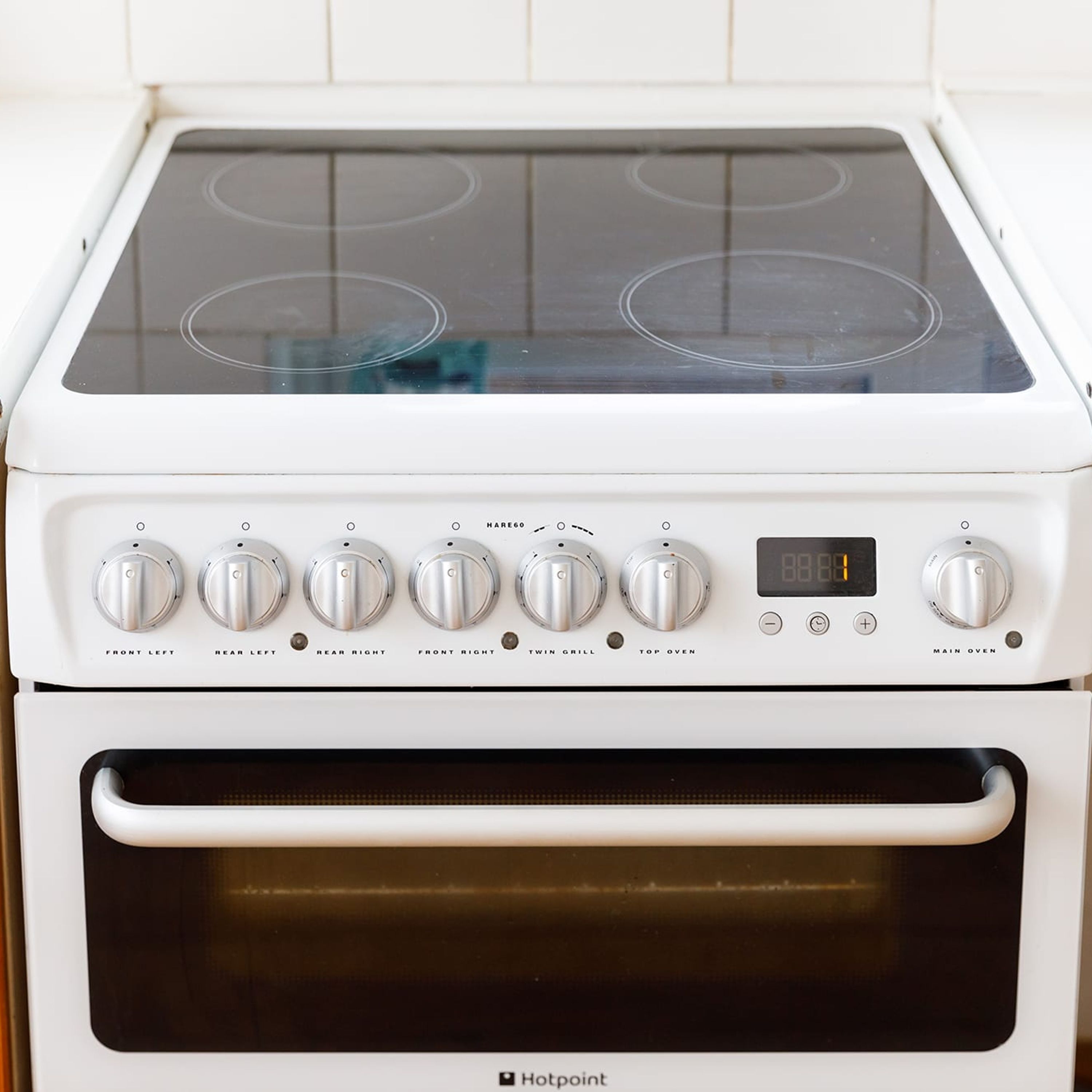 Une cuisinière Hotpoint blanche, dotée de six boutons et d’un écran numérique.