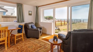 Ein Wohnzimmer mit Sofa, Sessel, Tisch und Meerblick durch große Fenster.