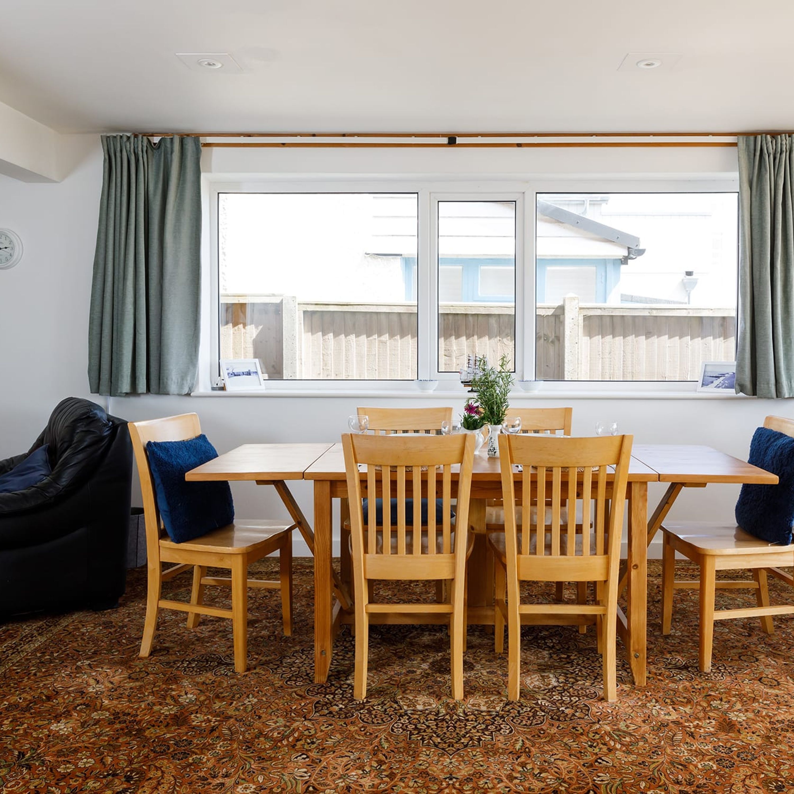 Un comedor con mesa y sillas de madera, alfombra estampada y una ventana con cortinas.