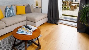A modern living room with a sectional sofa, a round wooden coffee table, and a large sliding glass door leading to an outdoor patio. - Charming 3bd Townhouse Right in the City Centre (Chichester)