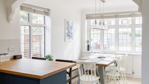 A modern kitchen with a central island, white cabinetry, and a large window providing natural light. - Bright Modern 4 br House 100 Metres From Beach (Chichester)