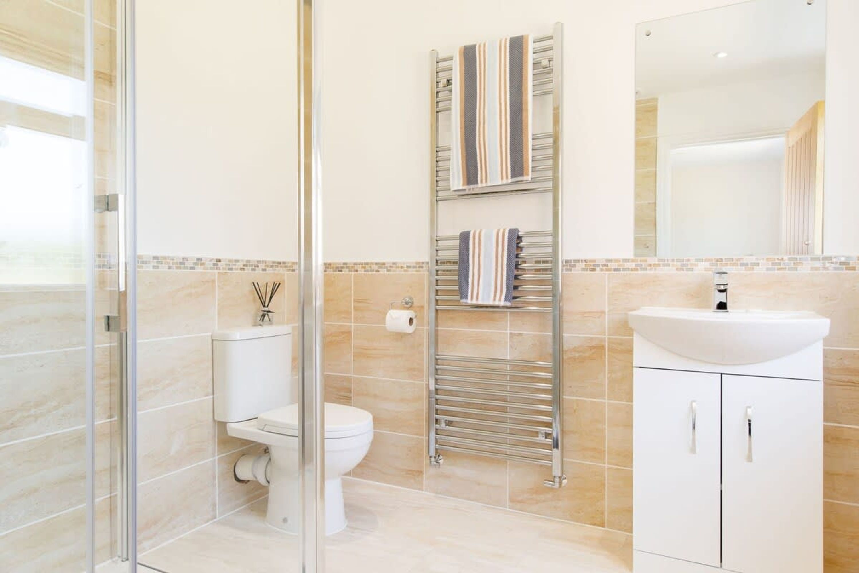 A modern bathroom with a glass shower enclosure, a toilet, a towel rack with striped towels, and a white sink with a mirror above it.