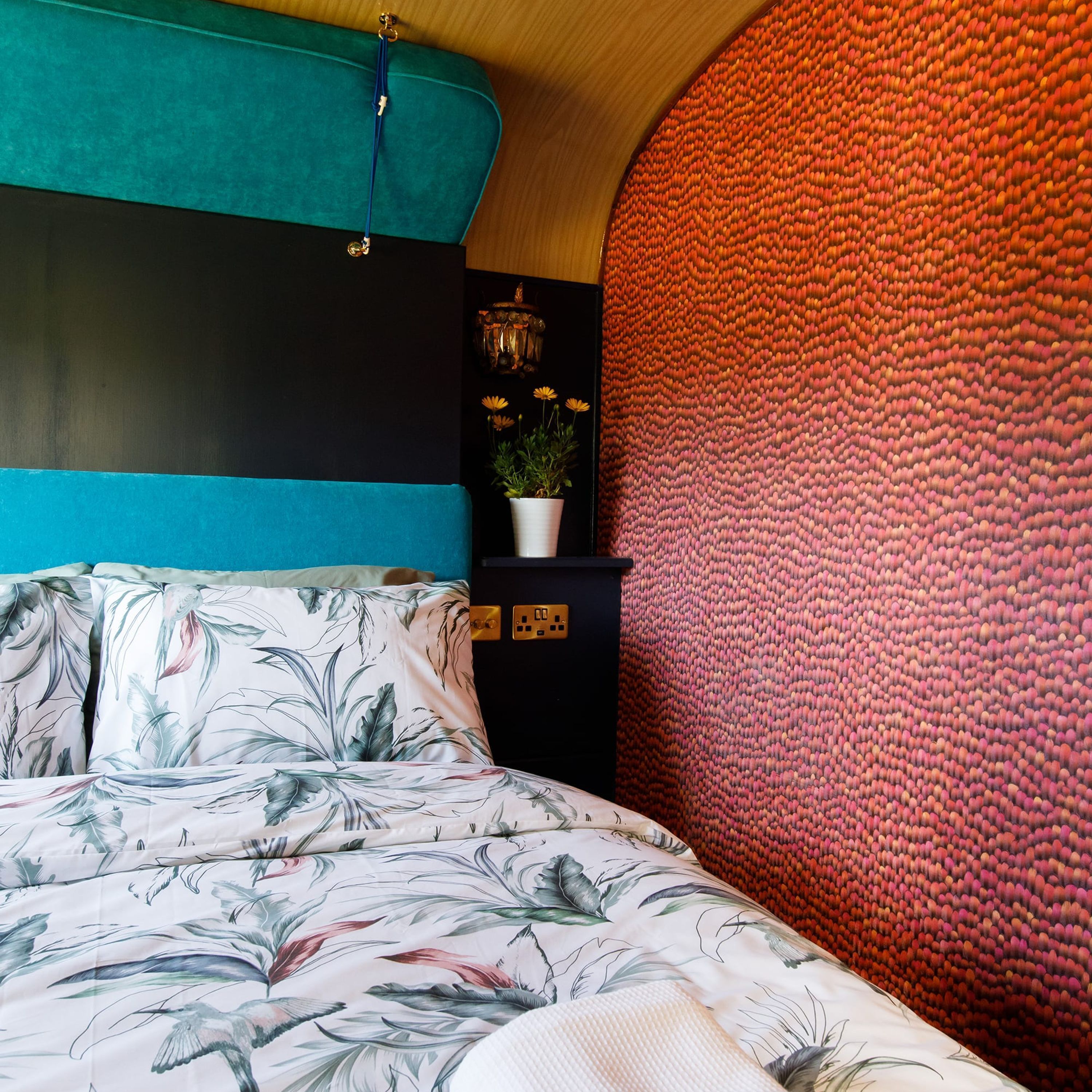 A bedroom with a bed, a potted plant, and a wall with a textured pattern.
