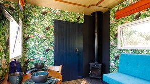 A cozy room with a wooden dining table, a blue sofa, a black stove, and a door with a tropical wallpaper.