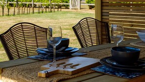 An outdoor dining area with two chairs, a table set with plates, bowls, and wine glasses.