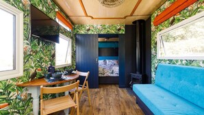 A compact room with a wooden floor, a blue sofa, a dining table with chairs, and a bed with a blue headboard.