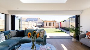 Uma sala de estar moderna com uma mesa de centro de vidro, um sofá azul e vista para um quintal com banheira de hidromassagem e painéis solares.