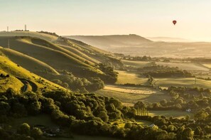 A landscape with rolling hills, a hot air balloon in the sky, and a distant view of a town. - Luxury Designer Coastal Home for 10 With hot tub (Chichester)