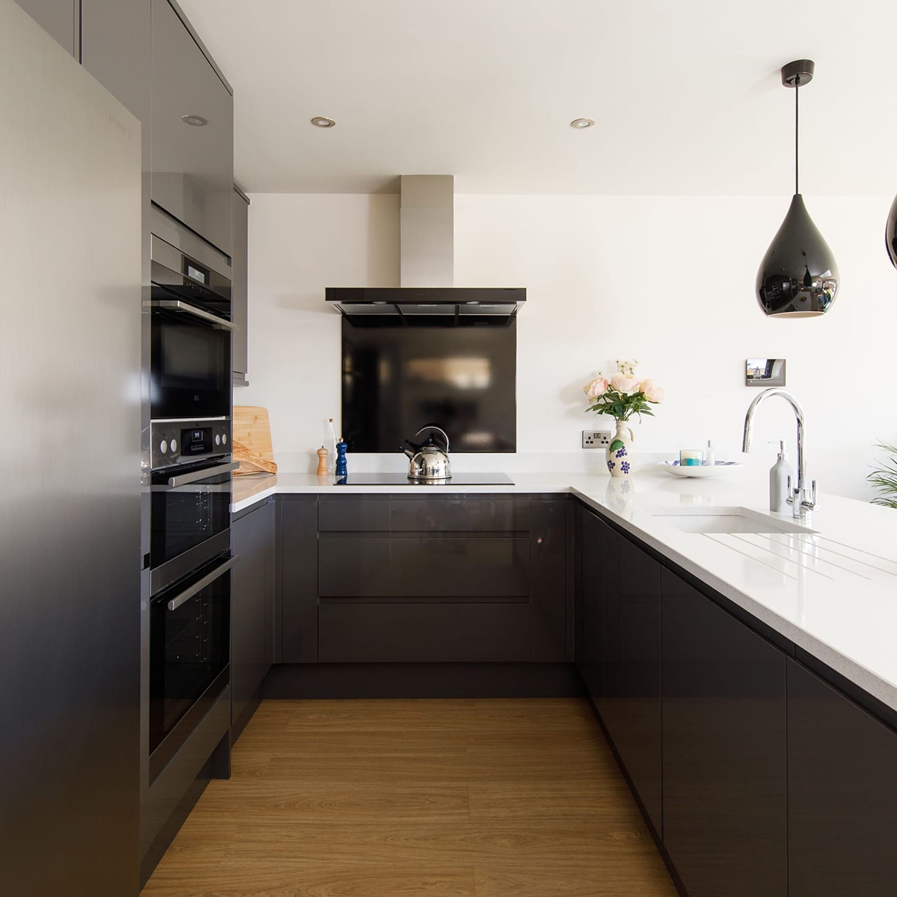 Een moderne keuken met donkere kastjes, een wit aanrecht en een roestvrijstalen afzuigkap.