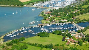 Vista aérea de uma marina com muitos barcos atracados, rodeada por campos verdes e edifícios residenciais.