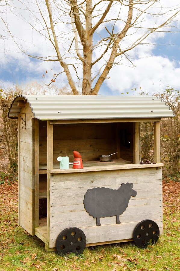 A wooden structure with a metal roof, a sheep cutout, and a small shelf with a pot and a red object.