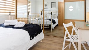 Une chambre moderne avec un grand miroir, un lit recouvert de linge de lit blanc, un bureau en bois et une chaise blanche.