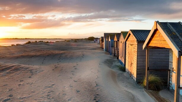 Une rangée de cabanes en bois bordant une plage de sable, avec des empreintes de pas menant à ces cabanes.