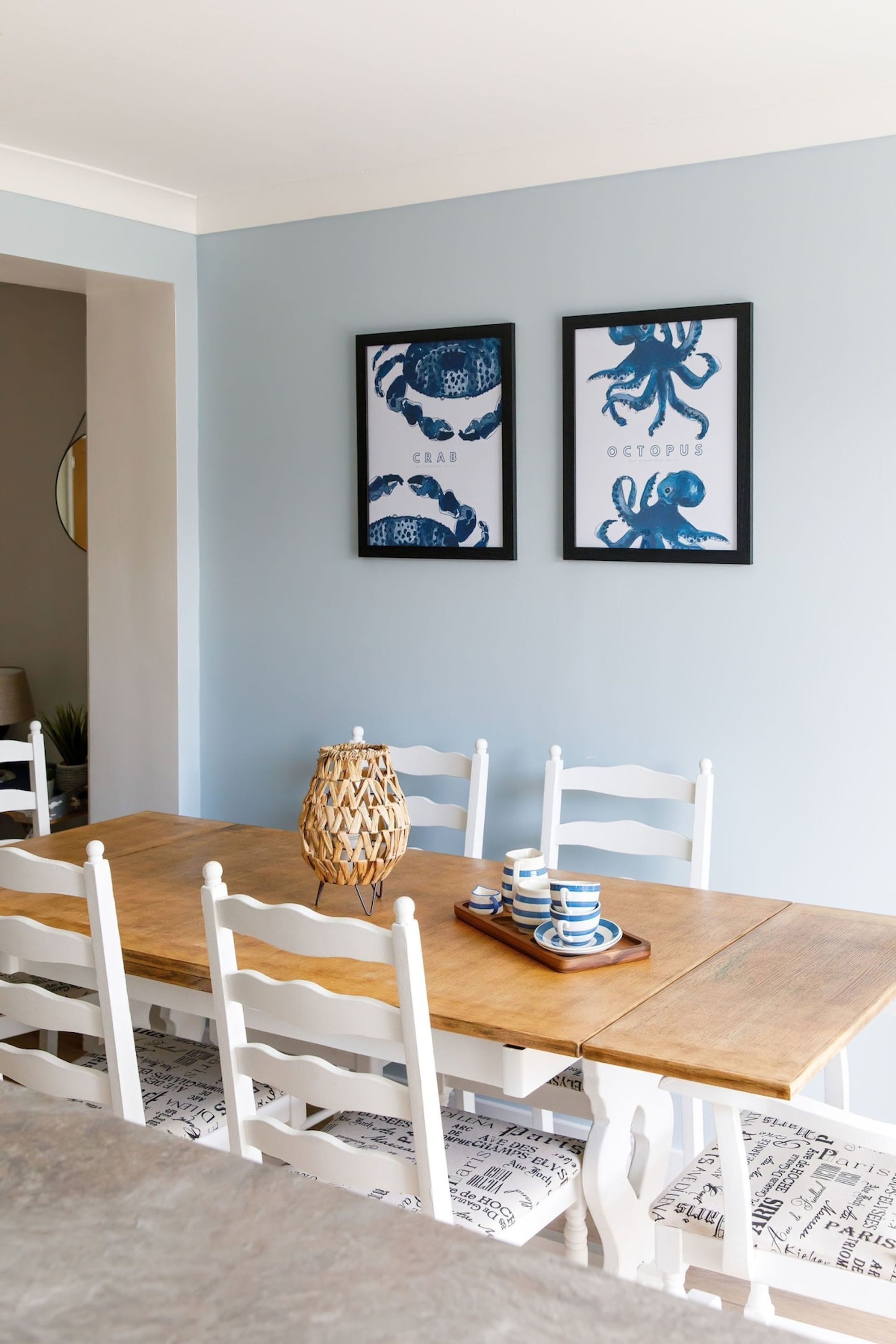 A dining area with a wooden table, white chairs, and two framed wall art pieces.