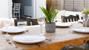 Une table à manger dressée avec des assiettes, des couverts et des verres à vin, agrémentée d’une plante en pot et d’un pot décoratif.