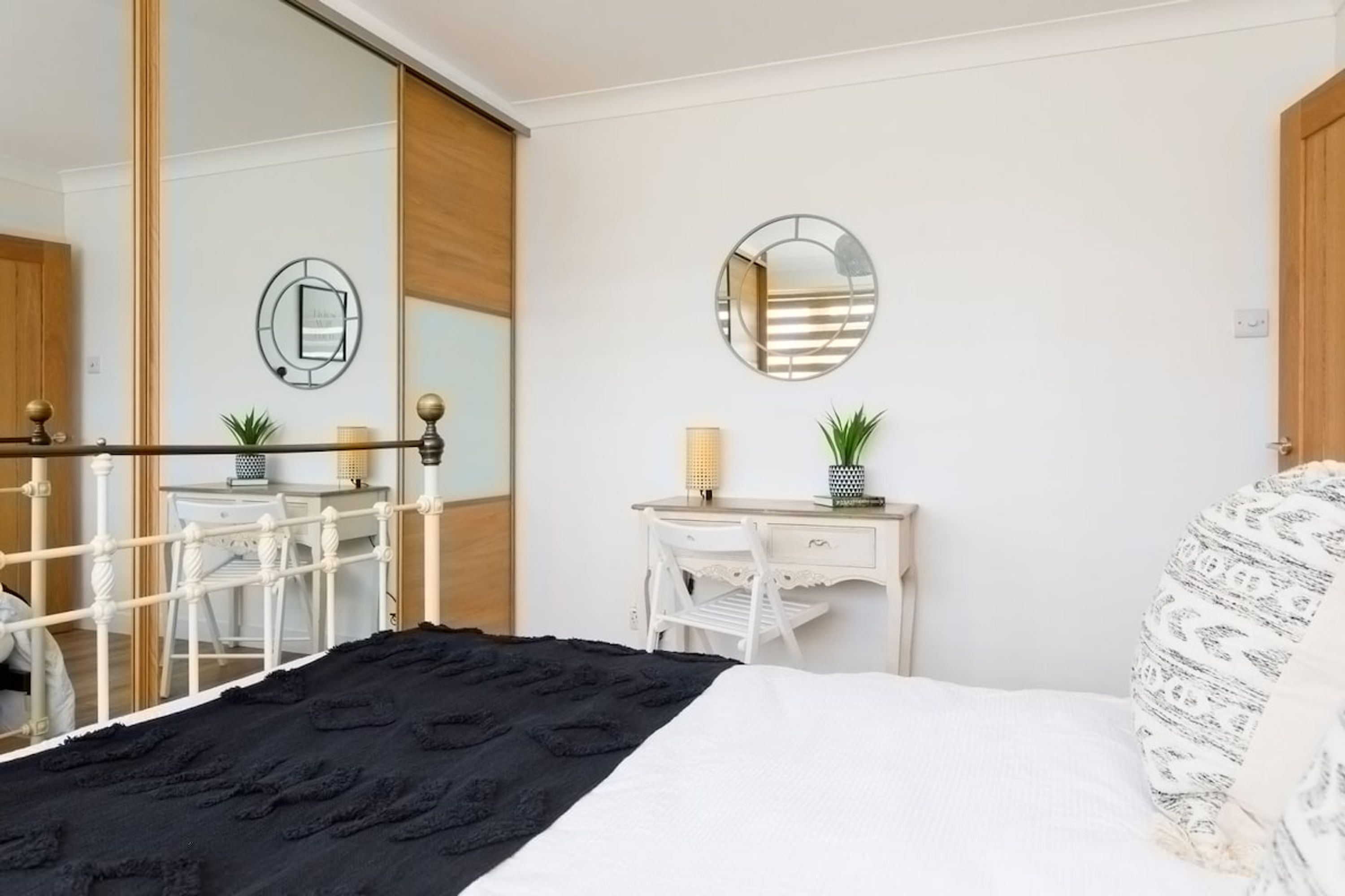 Une chambre à coucher avec un lit, un bureau blanc, deux miroirs et une porte coulissante.